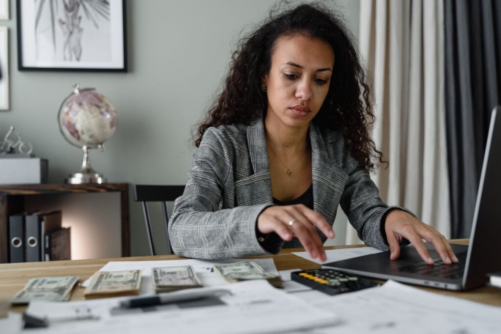 Woman counting US dollar notes next to a laptop